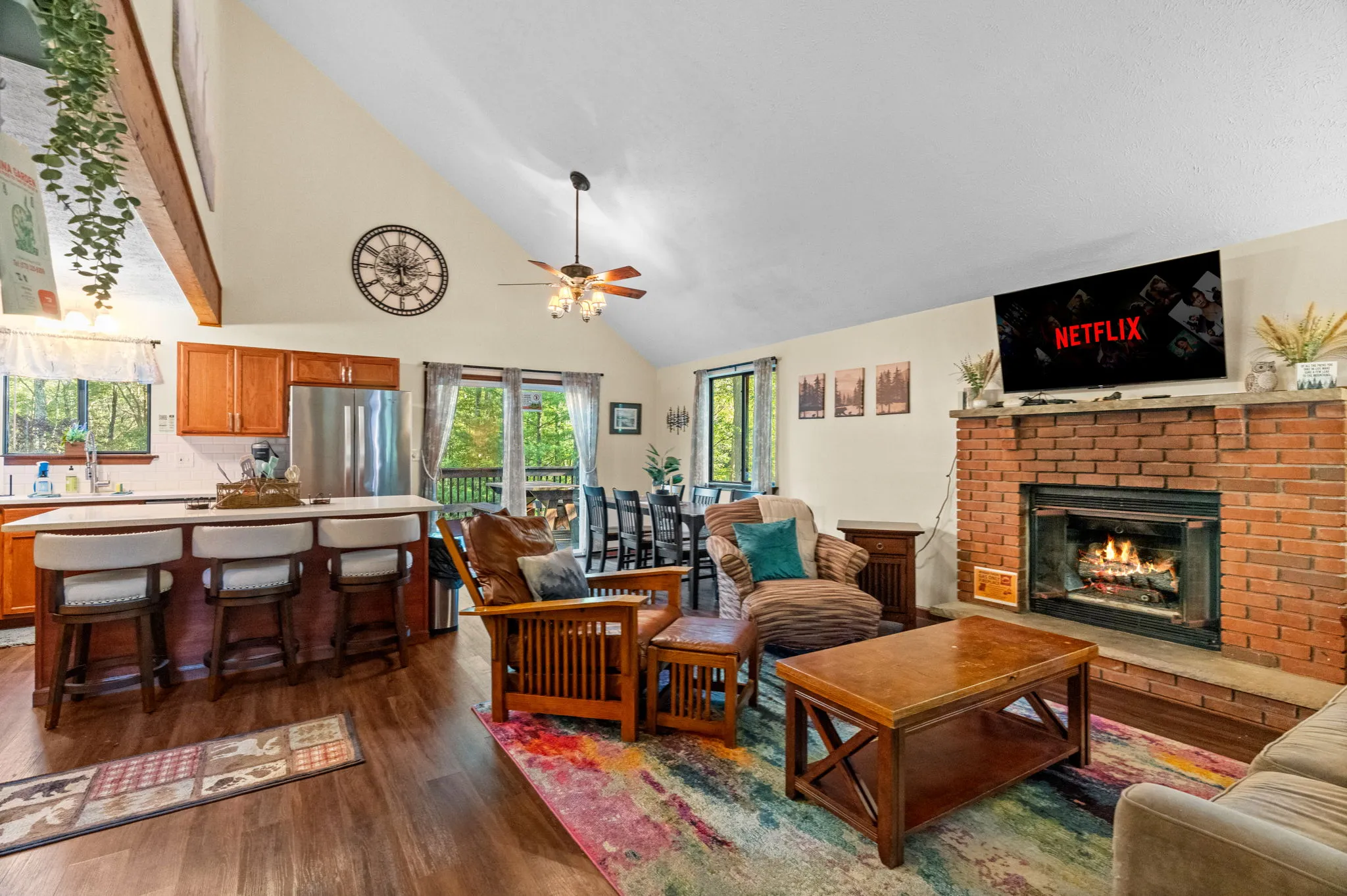 Open living room with brick fireplace, kitchen island and cathedral ceiling